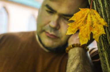 Adam karamsar bir portre düşünüyor, sonbahar parkında dikiliyor, bir akçaağaç yaprağına seçici odaklanıyor..