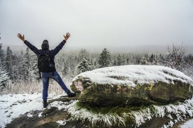 Sırt çantalı, sırt çantalı, sırt çantalı turistin arkadan görünüşü alacalı orman dağlarında karla kaplı ve bulutlu gökyüzü arka planında kollarını kaldırmış. Eller yukarı.. 