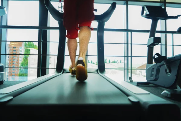 Theme of sport and weight loss. Close-up of the feet of a young strong man in a white and black sneakers on a simulator, running in the gym