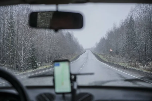 Satellite navigation system mount in the salon of a modern car, with the background of beautiful winter road in the woods. way perspective.