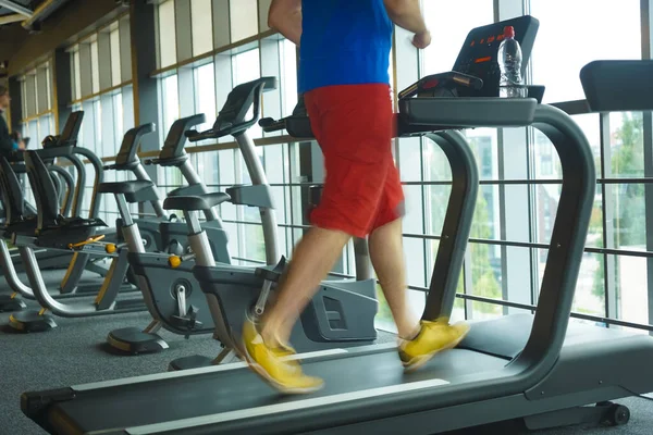 Feet with sneakers of male runner. jogger running on treadmill indoors in action - with motion blur.