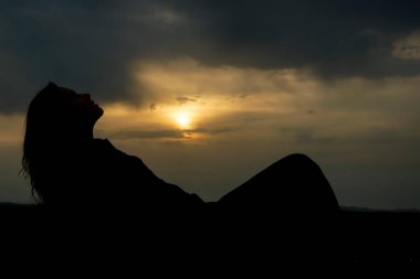 Genç ve güzel bir kızın silueti kumların üzerinde uzanıyor ve günbatımının tadını çıkarıyor, karada bir kadın figürü, yaz tatili kavramı.
