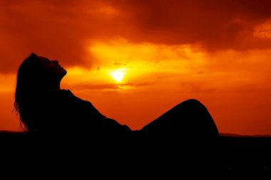 Genç ve güzel bir kızın silueti kumların üzerinde uzanıyor ve günbatımının tadını çıkarıyor, karada bir kadın figürü, yaz tatili kavramı.