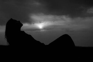 Genç ve güzel bir kızın silueti kumların üzerinde uzanıyor ve günbatımının tadını çıkarıyor, karada bir kadın figürü, yaz tatili kavramı.