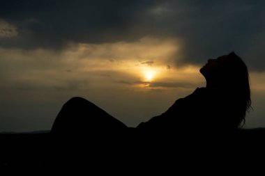 Genç ve güzel bir kızın silueti kumların üzerinde uzanıyor ve günbatımının tadını çıkarıyor, karada bir kadın figürü, yaz tatili kavramı.