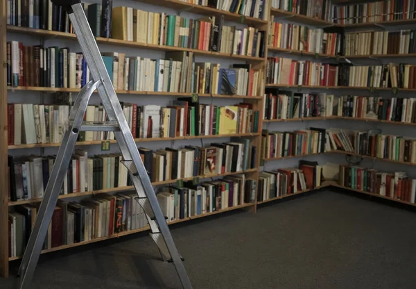 workplace with library and interior design objects. Bookshelf in the library, in the form of blurred books lined up on shelves. Stairs for picking up a book is high.