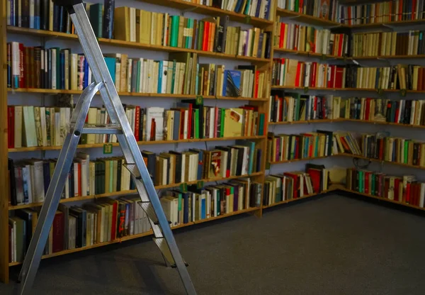 workplace with library and interior design objects. Bookshelf in the library, in the form of blurred books lined up on shelves. Stairs for picking up a book is high.