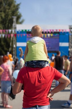 Genç çocuk babasının omzunda oturuyor. Mutlu evlat tatilde omuz gezintisi yapıyor, fotokopi odası. Oğlum uzaklara bakıyor. geri, arka plan.