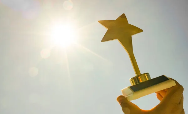 Golden star award in male hand on blue sunny sky  background. sunshine.