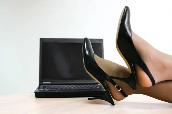 female legs in the high heels, on a table with a laptop. empty screen. no face.womans legs in fashionable shoes on desk with laptop. Businesswoman relaxing at the desk. Female office worker resting during working