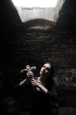 Dini hayat kavramı. Rahibe arşivde dua ediyor. Karanlık ortaçağ manastırında. Taş duvar arkasında taş haç tutan orta yaşlı bir kadın.