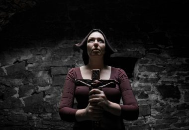 Dini hayat kavramı. Rahibe arşivde dua ediyor. Karanlık ortaçağ manastırında. Taş duvar arkasında taş haç tutan orta yaşlı bir kadın.