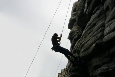 Dağın tepesindeki bir uçurumun tepesindeki dağcı silueti. Ekstrem sporlar. Kaya boyunca tırmanan adam zorlu bir yola giriyor.