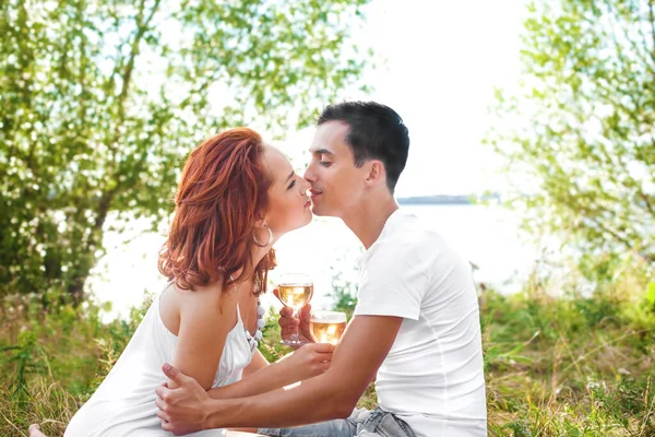 喜欢在日落时在河边喝酒或喝香槟的夫妻 一个男朋友和一个女孩在一个浪漫的约会 坐在和喝香槟的眼镜 恋爱中的夫妻男人和女人接吻 — 图库照片