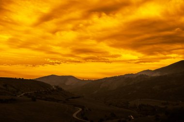 Arkaplanda Karlı Tepeler olan kıvrımlı Serpentine High Mountains Yolu. Yeşil Tepelerin Arasındaki Yılan Yolu. Dağlarda gün batımı. 