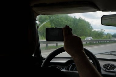 Dikiz aynasının fotoğrafını ya da videosunu çekmek için cep telefonlu bir adamın silueti. Bir el direksiyonu çevirir.