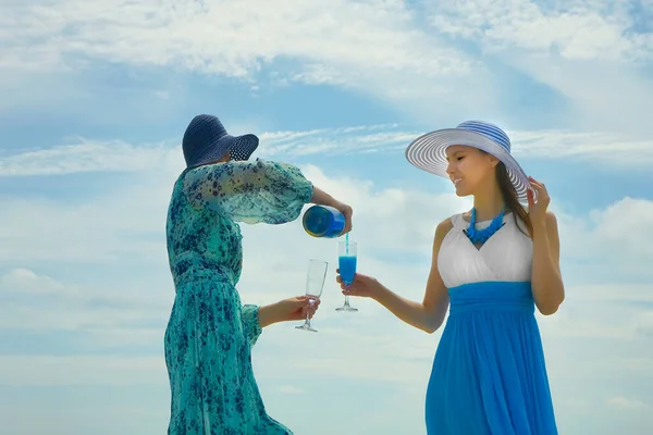 夕方のドレスを着て青い曇り空の背景に立っている若い女性は カメラの大声で陽気に笑う眼鏡に青いシャンパンを注ぐボトルを保持 — ストック写真