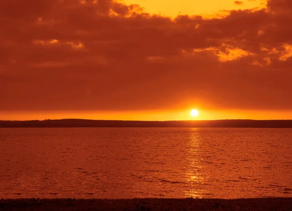 Dark orange sea surface at sunset. Sun setting down on the horizon. A beautiful sunset. An image of sun going down behind a big lake. Image has a strong vintage effect applied.