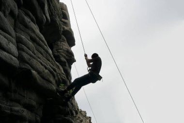 Dağın tepesindeki bir uçurumun tepesindeki dağcı silueti. Ekstrem sporlar. Kaya boyunca tırmanan adam zorlu bir yola giriyor.