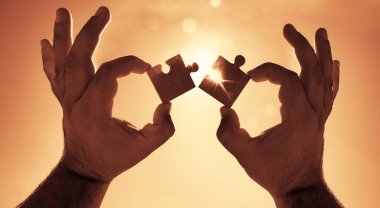 Gökyüzü arka planında yapboz parçaları olan eller.  