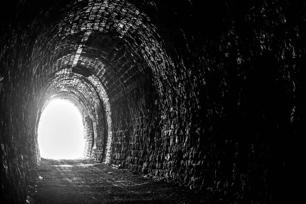 Old creepy underground stone tunnel. Halloween Locations. Dark stone tunnel illuminated by a beam of light. A light in the end of a tunnel