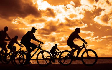 Boşluk. Gün batımında bisiklete binen sportif arkadaşlar. Bisikletçiler sahil boyunca gidiyor. Doğa arka planında spor.