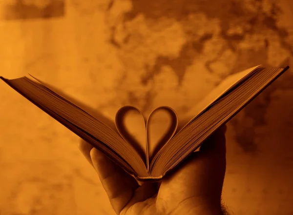 pages of a book curved into a heart shape. globe map on background. male hand holding book