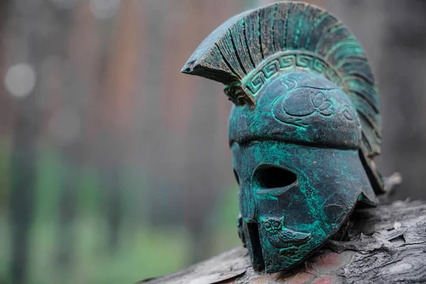 Historical Replica Spartan Warrior Helmet on pine forest background. Close up view of small miniature roman helmet