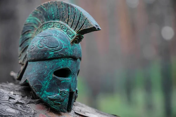 Historical Replica Spartan Warrior Helmet on pine forest background. Close up view of small miniature roman helmet