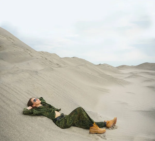 砂の上に寝そべってる武器のない制服の女が一人 砂漠を背景にした軍の衣装を着た一人のゴージャスな若い女性 ロシアのカーキの制服 — ストック写真