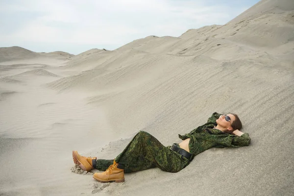 砂の上に寝そべってる武器のない制服の女が一人 砂漠を背景にした軍の衣装を着た一人のゴージャスな若い女性 ロシアのカーキの制服 — ストック写真