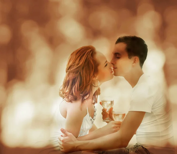 Loving couple drinking wine or champagne at sunset on a river bank. A boyfriend and a girl on a romantic date, sitting and drinking champagne from glasses. couple in love. man and woman kissing