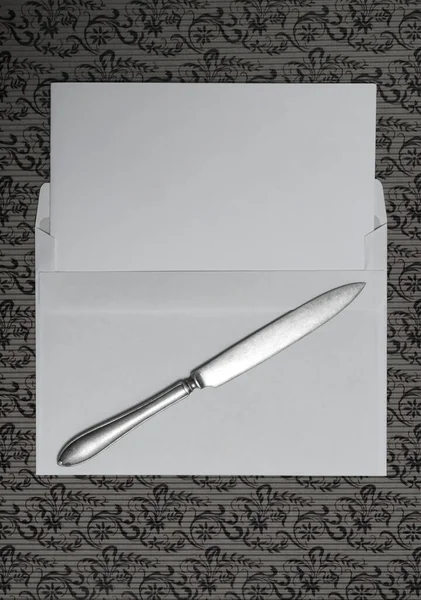 Blank paper with knife and letter  on pattern. A top down view of a white envelope and a letter opener on a paper surface.