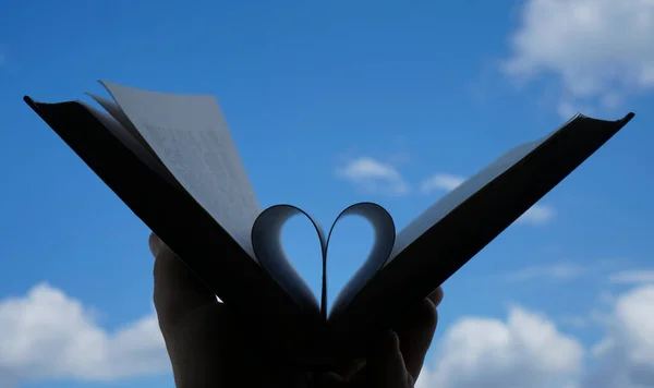 Book lover or love reading concepts. Male hand holding book with heart shape page folded. blue sky background.