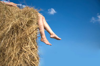 Kadın bacakları, saman balyasında dinlenen genç bir kadın. Yüzü yok. Tanımlanamayan kişi