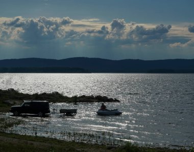 Motorlu sürat teknesi kalkışı silueti, pistteki siyah araba römorkuna tekne koyan bir adam.