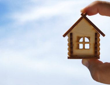Erkek eli, mavi güneşli gökyüzünde ahşap ev oyuncağı modelinin arasında. Yazı için boş kopyalama alanı 