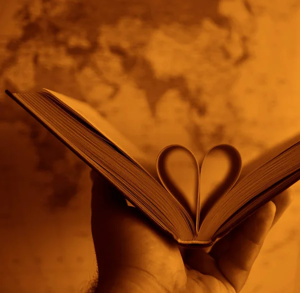 pages of a book curved into a heart shape. globe map on background. male hand holding book