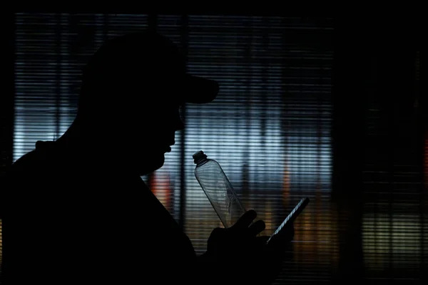 Sylwetka Mężczyzny Pijącego Plastikowej Butelki Przezroczystego Szkła Używającego Telefonu Komórkowego — Zdjęcie stockowe