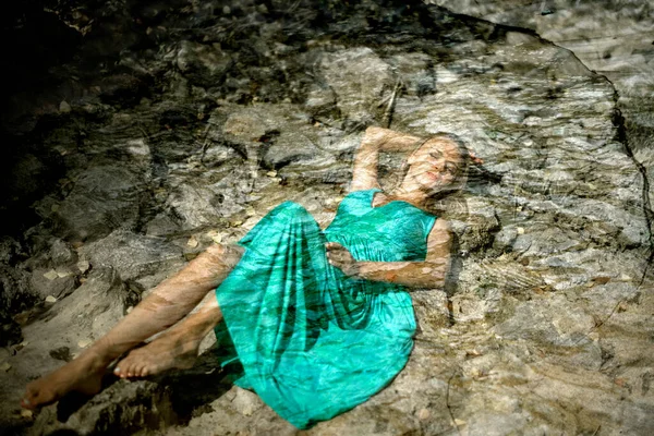 girl is drowned under water. blonde woman wearing a blue dress. sleep beauty charming sea princess resting on wet stones, girl in blue long tender dress lies in cold waterl hands under head hair, young female