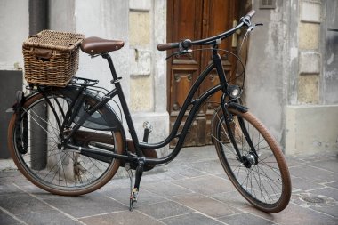Kahverengi ya da sarı ahşap kapının yanında eski tarz siyah bisiklet standı. gri beton arka plan. Hasır kutu. İNNSBRUCK, AUSTRIA