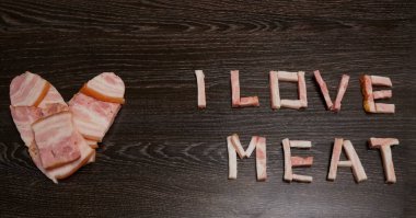 Bir kalp oluşturan İspanyol jambonu yığını. Siyah ahşap arka plan. Kalp şeklinde dilimlenmiş domuz parçaları et sevgisini sembolize eder. Ete bayılırım..