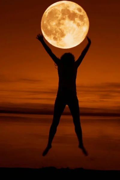 full red moon above head and between hands. jumping and Dancing woman silhouette on the seaside during twilight. Silhouette of a girl jumping at sunset on the beach. summertime srason