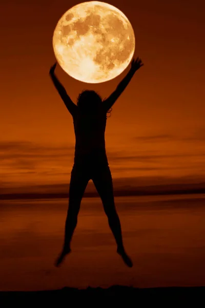 full red moon above head and between hands. jumping and Dancing woman silhouette on the seaside during twilight. Silhouette of a girl jumping at sunset on the beach. summertime srason