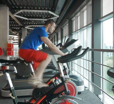 Spor salonunda bisiklet kullanan kaslı bir adam. Spor salonunda bisiklet kardiyo çalışması. yan görünüm.