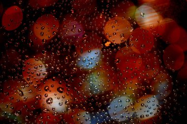 Kapatın ve cam pencereye yağmur damlalarının makro görünümü ve kırmızı ve sarı ışık bokeh yuvarlak ile bulanık arkaplan. 