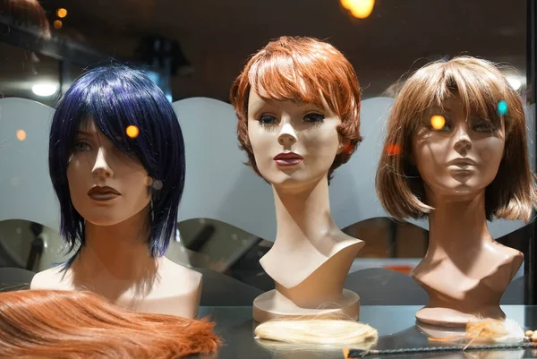 Row of Mannequin Heads with Wigs on the Shelf. night scene. Mannequins with ginger style wigs in  hair salon