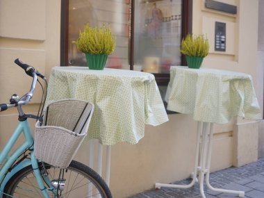 Modern bir kafenin yanında beyaz sepeti olan mavi bir bisiklet. Yeni rahat cadde. Çiçekli masalar. Salzburg, Avusturya.
