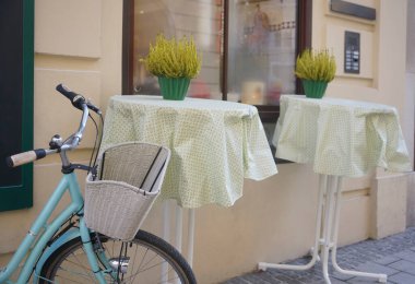 Modern bir kafenin yanında beyaz sepeti olan mavi bir bisiklet. Yeni rahat cadde. Çiçekli masalar. Salzburg, Avusturya.