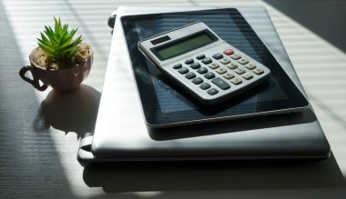 Bilgisayar, tablet bilgisayar, akıllı telefon, hesap makinesi ve metin için fotokopi alanı olan yeşil bitkiyle birlikte çalışma alanı çalışma masası en üstte. Güneşli ışık ve gölge. Jaluzili bir pencereden gelen güneş ışığı